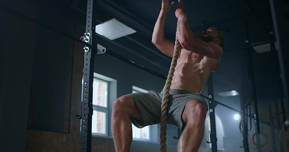 在健身房一个强壮的泵男爬上绳子爬到顶端视频的预览图