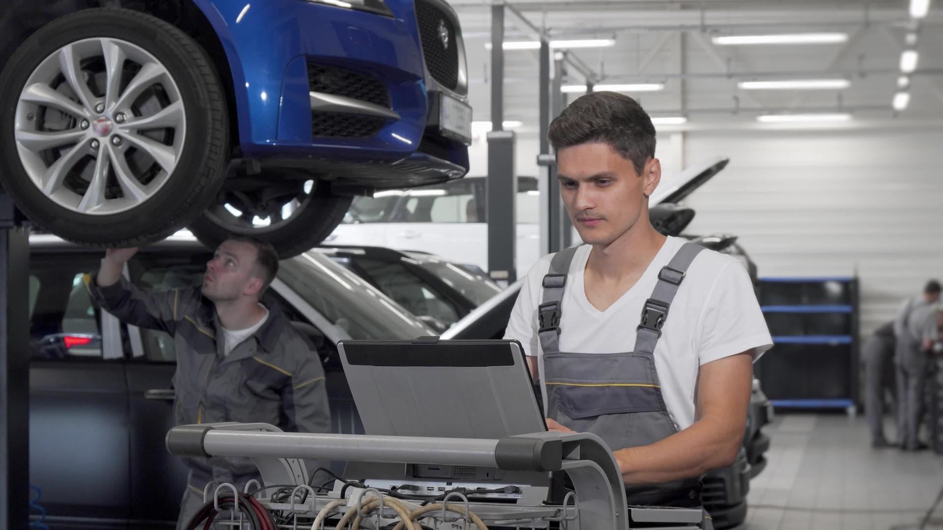 年轻的汽车机械工人在车库里使用膝盖电脑视频的预览图
