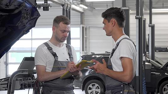 一名年轻的男子汽车机械师在车库里与同事交谈视频的预览图