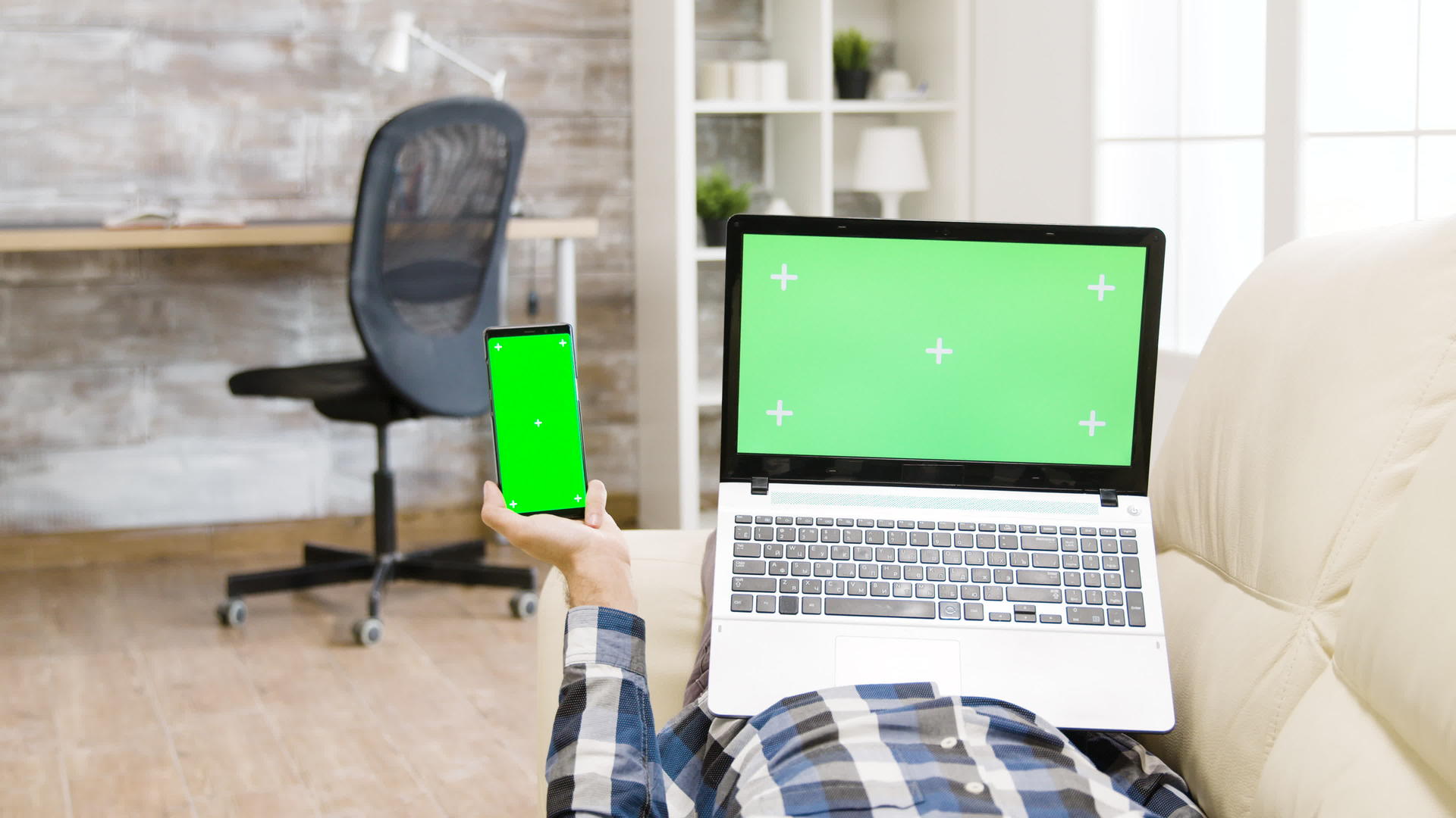 手持绿色屏幕智能手机和笔记本电脑的人躺在沙发上视频的预览图