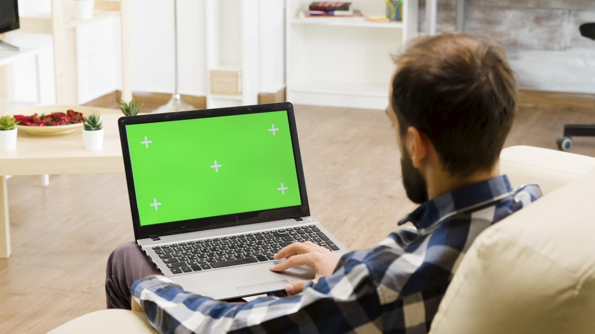 坐在沙发上的男人大腿上有一台绿色屏幕笔记本电脑视频的预览图