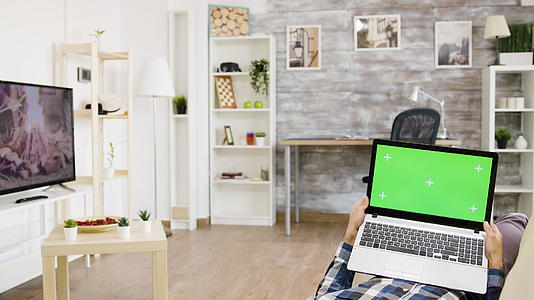 坐在沙发上的人在他的客厅里拿着一台绿屏笔记本电脑视频的预览图