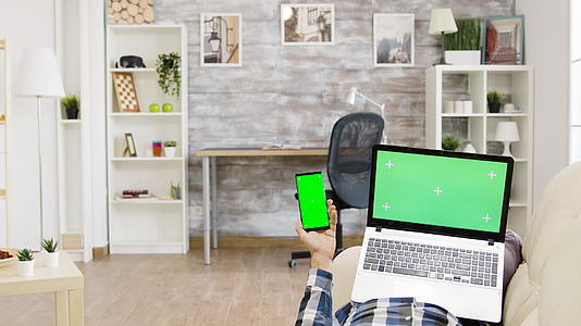 躺在沙发上的人手里拿着绿色屏幕笔记本电脑和智能手机视频的预览图
