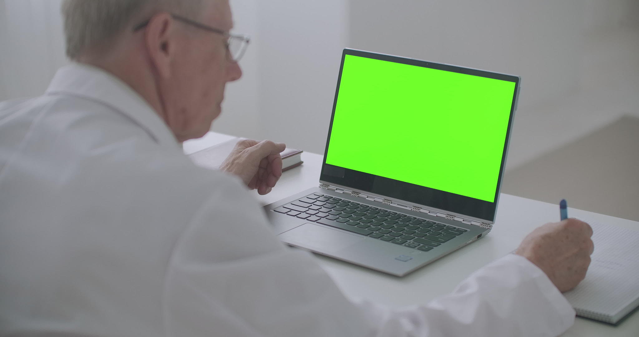 工作医生桌上有一个绿色屏幕的笔记本电脑那人正在看显示和显示视频的预览图