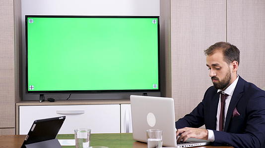 笔记本电脑上的商人类型和绿色屏幕Tv相邻视频的预览图