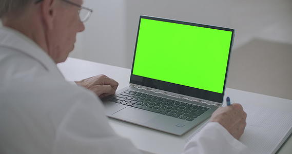 诊所治疗师桌子上有一个带有绿色屏幕的笔记本在线医生预约概念视频的预览图