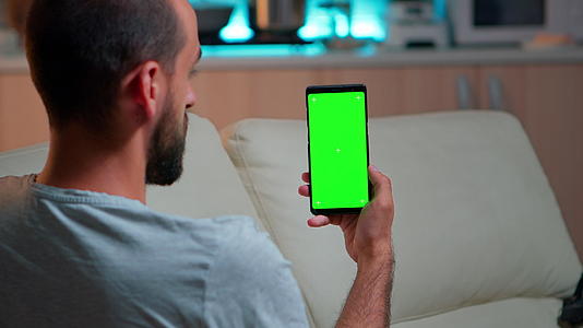 放松的男人看着智能手机模拟绿色屏幕染色仪键视频的预览图