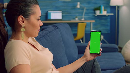 坐在客厅沙发床上的女性自由职业者看着孤立的智能手机视频的预览图
