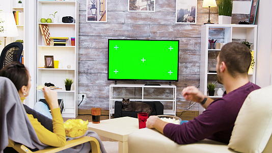 一对夫妇在家庭绿屏上看电视的后视图视频的预览图