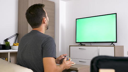 成年男子在大绿色模拟屏幕前在控制台上玩电子游戏视频的预览图