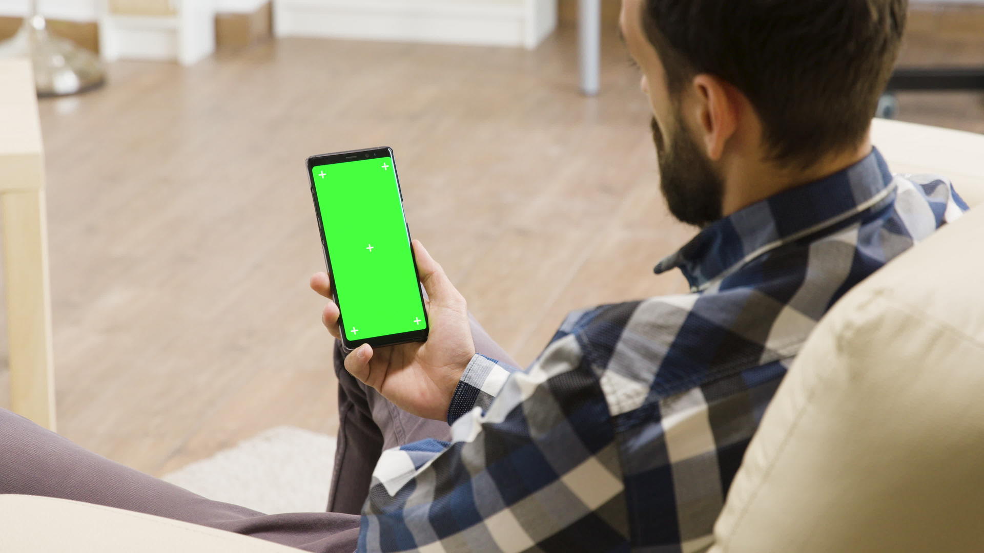 坐在沙发上的年轻人看着带有绿色屏幕的智能手机视频的预览图