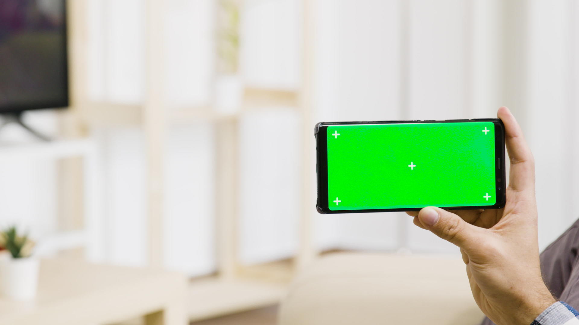 在现代明亮的客厅里男人手里拿着一个绿色的屏幕电话视频的预览图