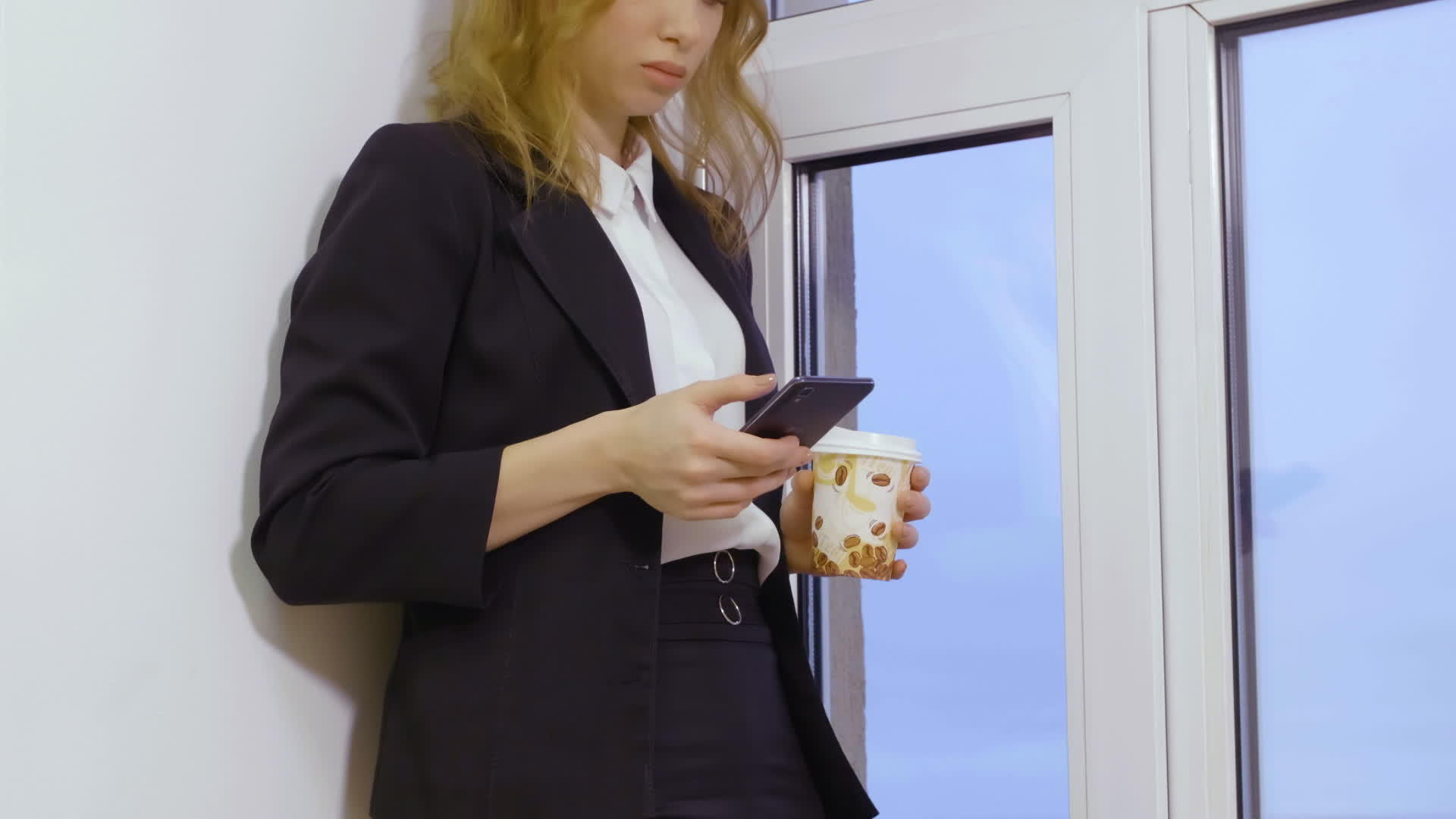 金发美女在商业办公室用手机拿着咖啡杯视频的预览图