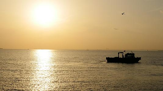 金色的晨光洒在海浪上一艘小船驶向远处的夕阳视频的预览图
