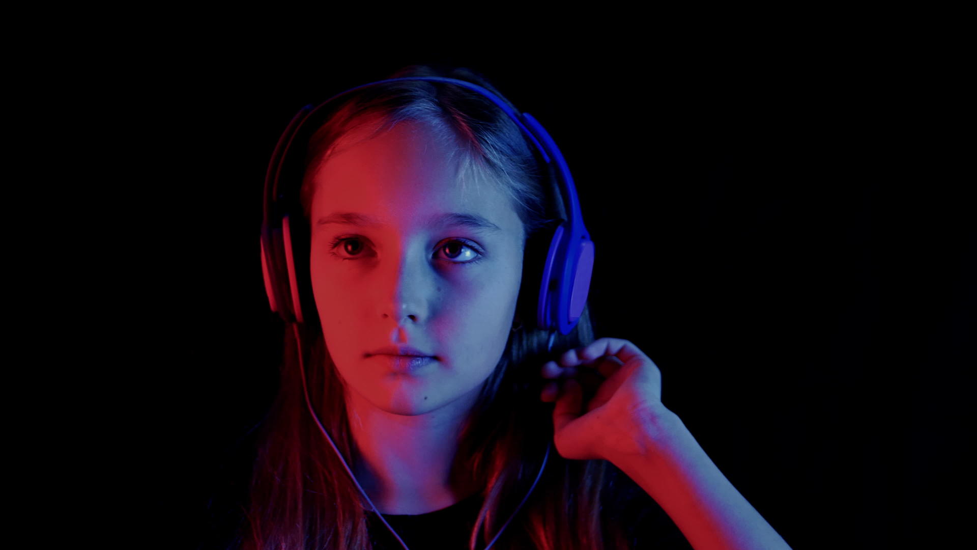 美丽的女孩在霓虹灯的黑暗房间里听音乐和耳机视频的预览图
