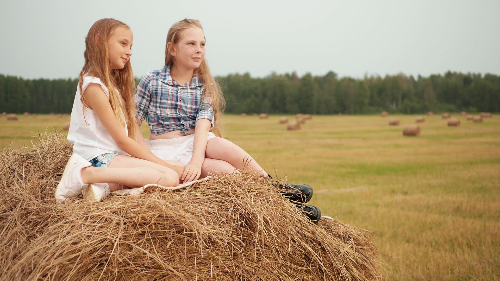 美丽的女孩坐在村里收割场的干草堆上视频的预览图