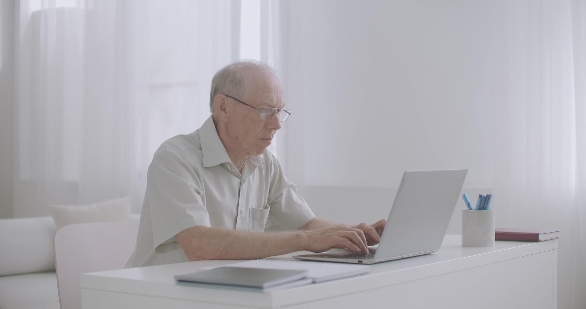 老年男性专家在家工作用笔记本电脑打字通过互联网发送视频的预览图
