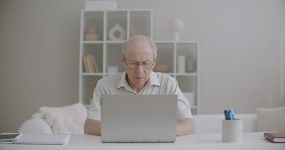 老人在家用笔记本电脑工作打字信息检查退休人员远程视频的预览图