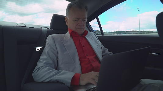 中年男子坐在车里的后座有笔记本电脑视频的预览图