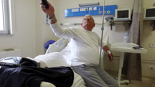 医院床上的高级男子手动换了电视手术视频的预览图
