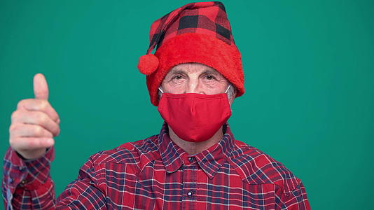 老人戴着圣诞红帽和医疗保护面具的肖像举起大拇指用拇指视频的预览图