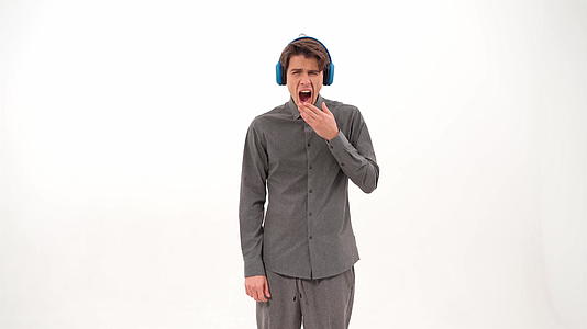 穿着灰色运动服的年轻人穿着蓝色无线耳机听音乐k录像片视频的预览图
