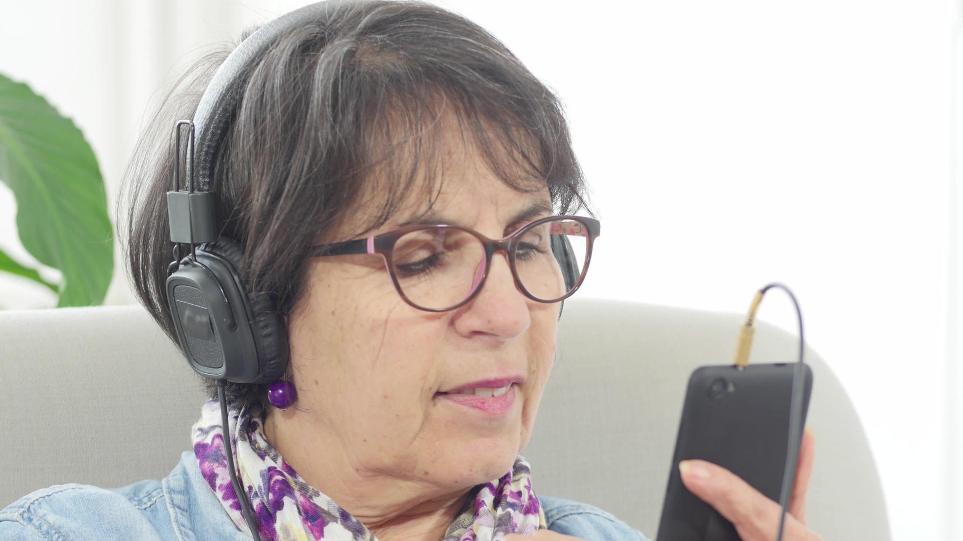 中年妇女在家用智能手机和耳机上听音乐视频的预览图