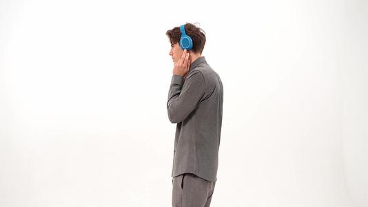 穿着灰色粗花呢或西装跳舞的年轻人侧身站着戴着蓝色无线耳机视频的预览图