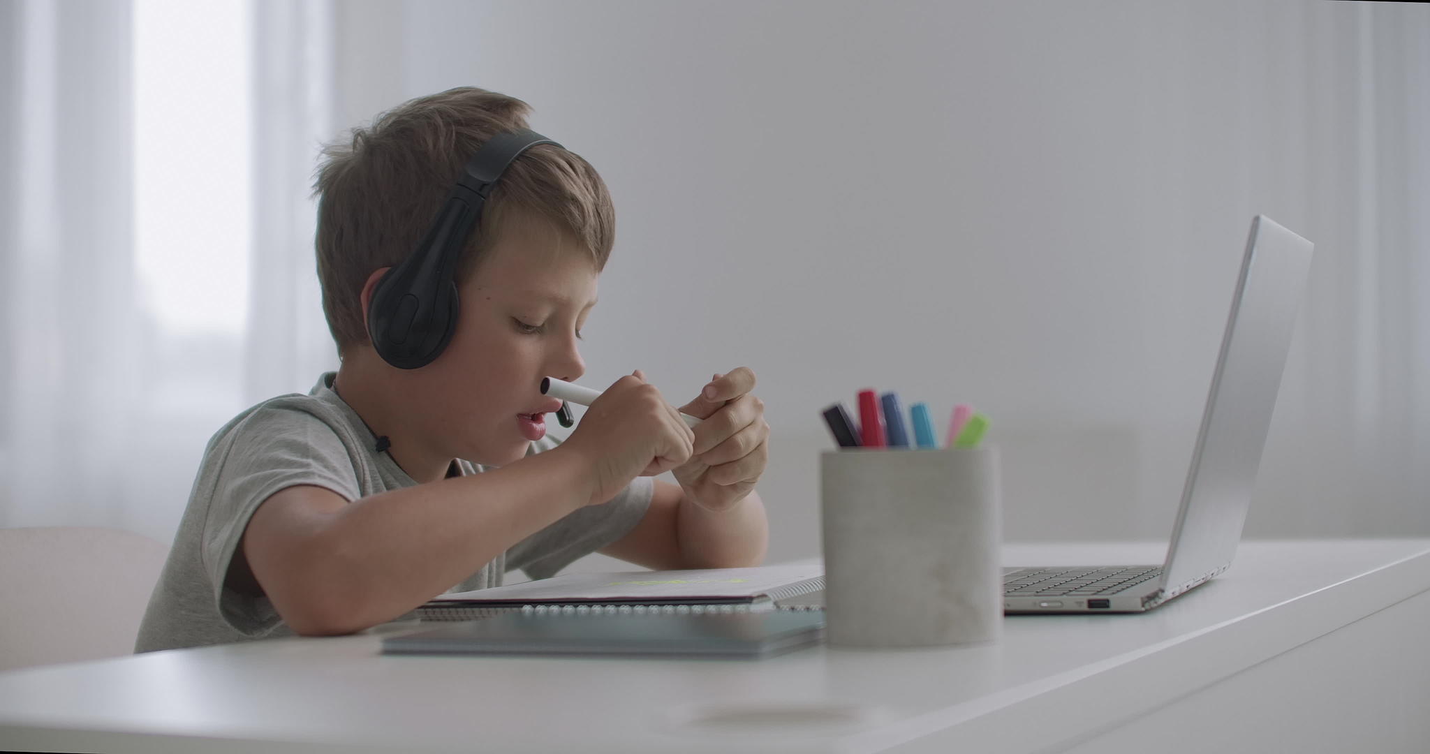 小男孩用耳机和麦克风在网上聊天看笔记本电脑和绘画视频的预览图