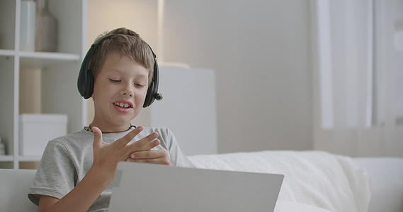 这个淘气的小男孩正在用笔记本电脑和活跃的孩子们在线聊天视频的预览图