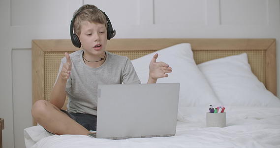 小男孩坐在夏令营里用笔记本电脑和父母聊天视频的预览图