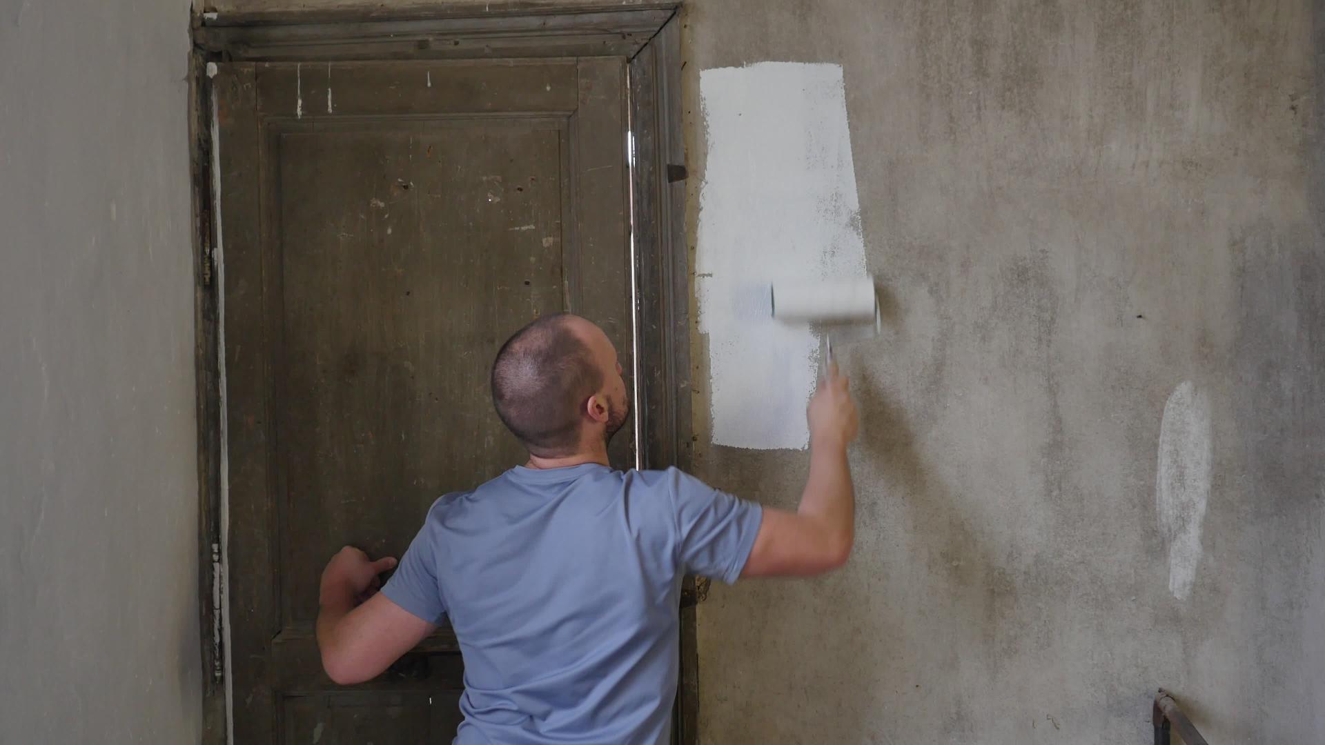 画家用油漆滚筒和桶在大空地上画墙的后视图视频的预览图