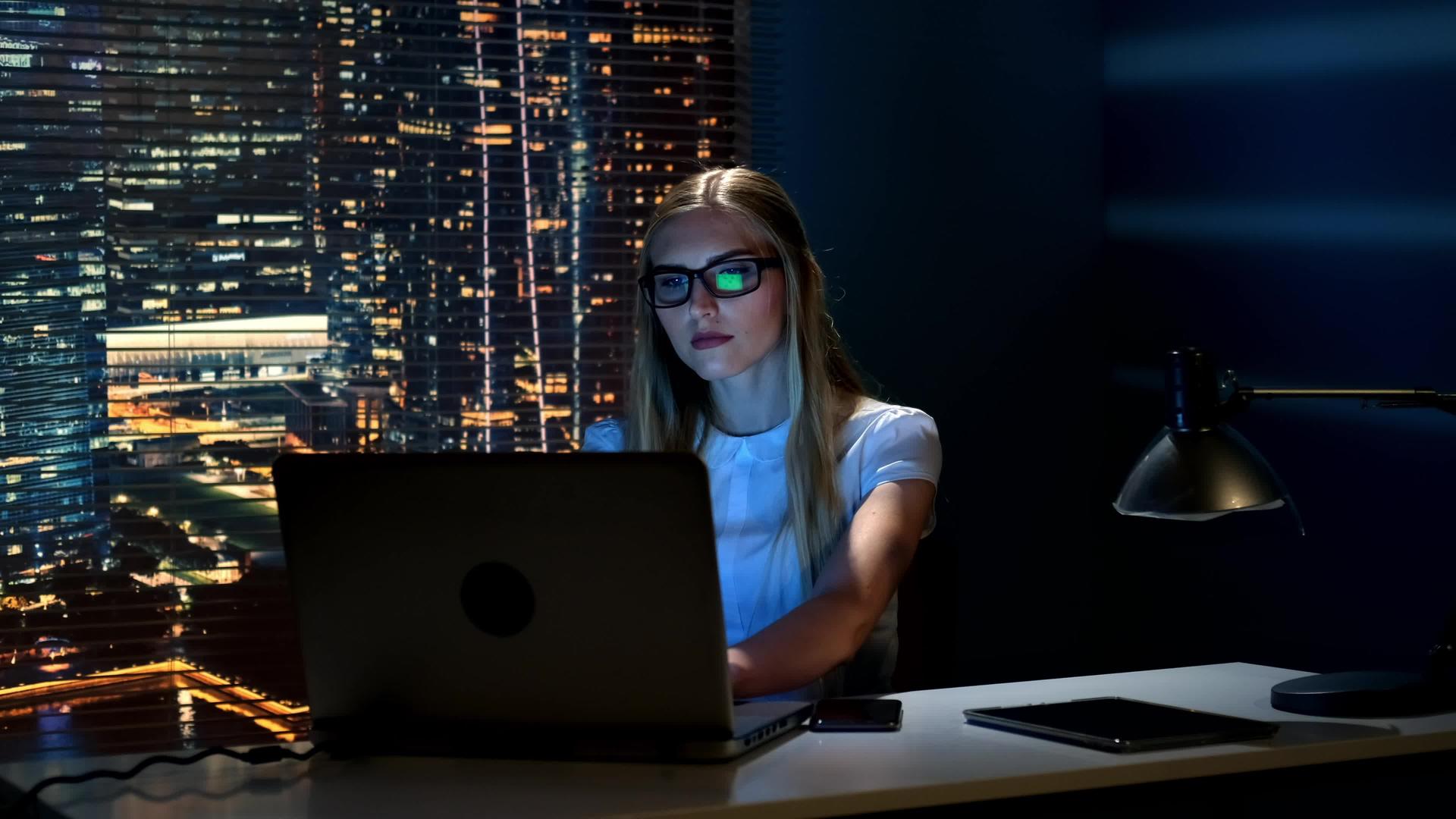 在电脑上工作时戴眼镜的聪明女性在智能手机上阅读信息视频的预览图
