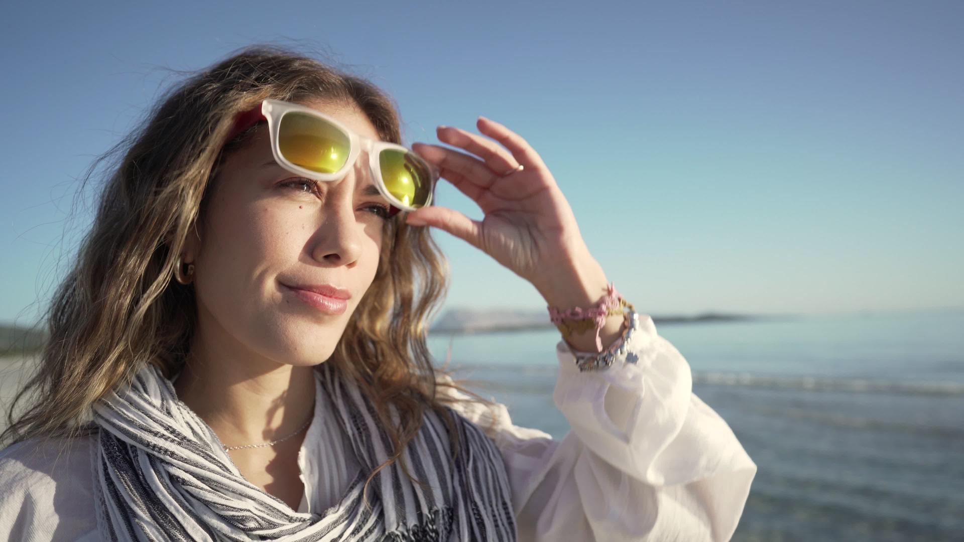 一个美丽的白人年轻的金发女郎在海滩上摘下太阳镜视频的预览图