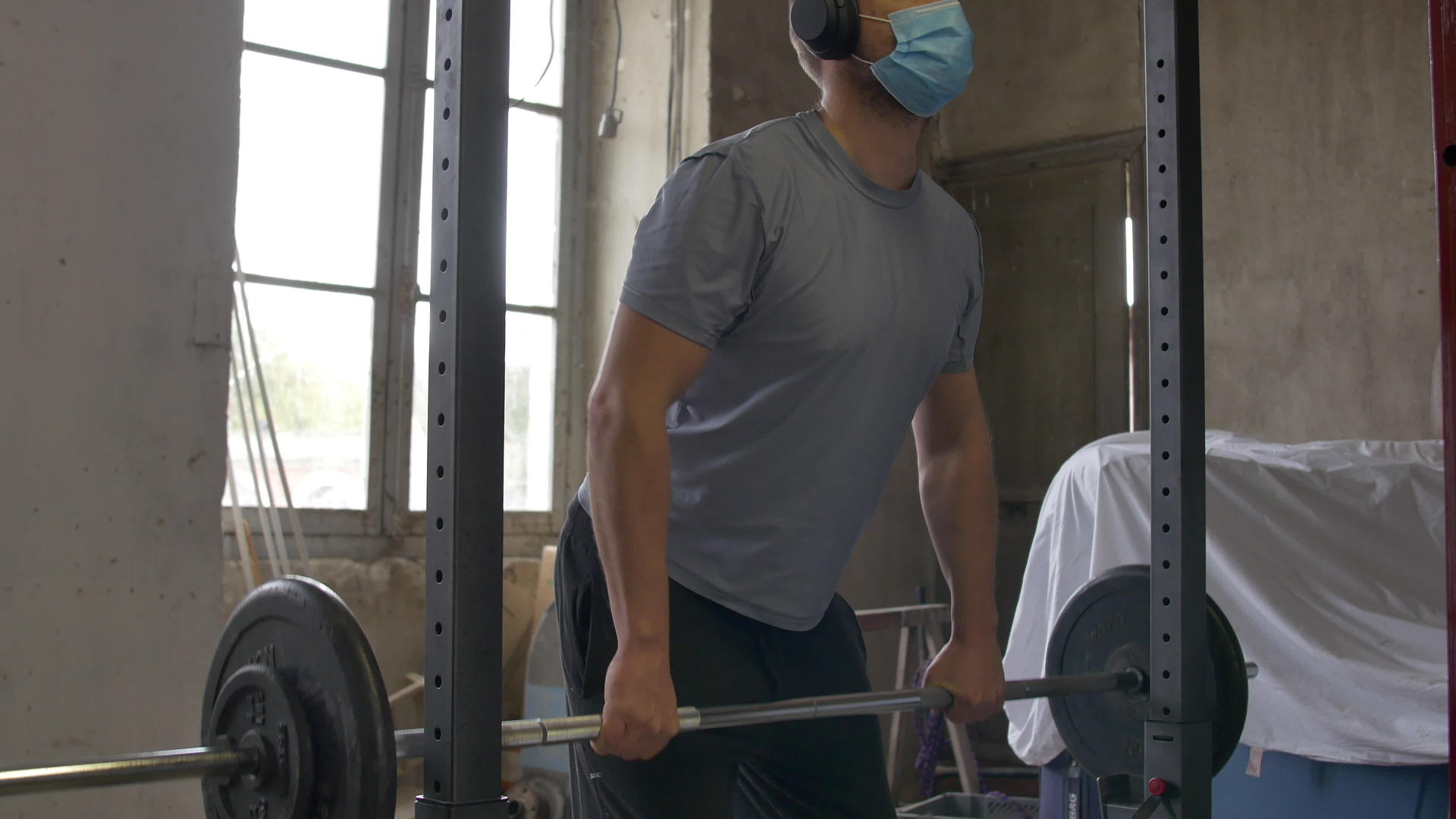 戴口罩的正常男性在封闭期间在家庭健身房锻炼背部视频的预览图