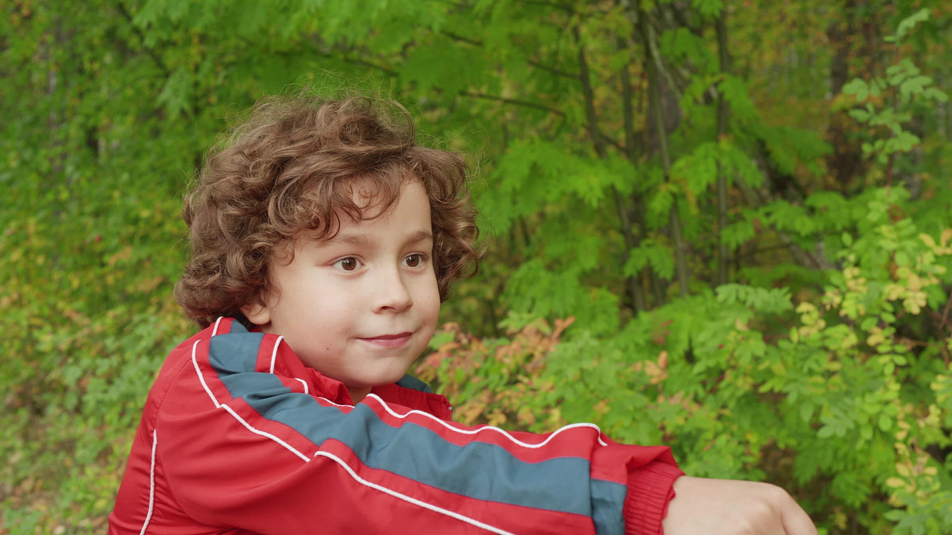 在绿色公园骑自行车的棕色头发的肖像卷发男孩视频的预览图