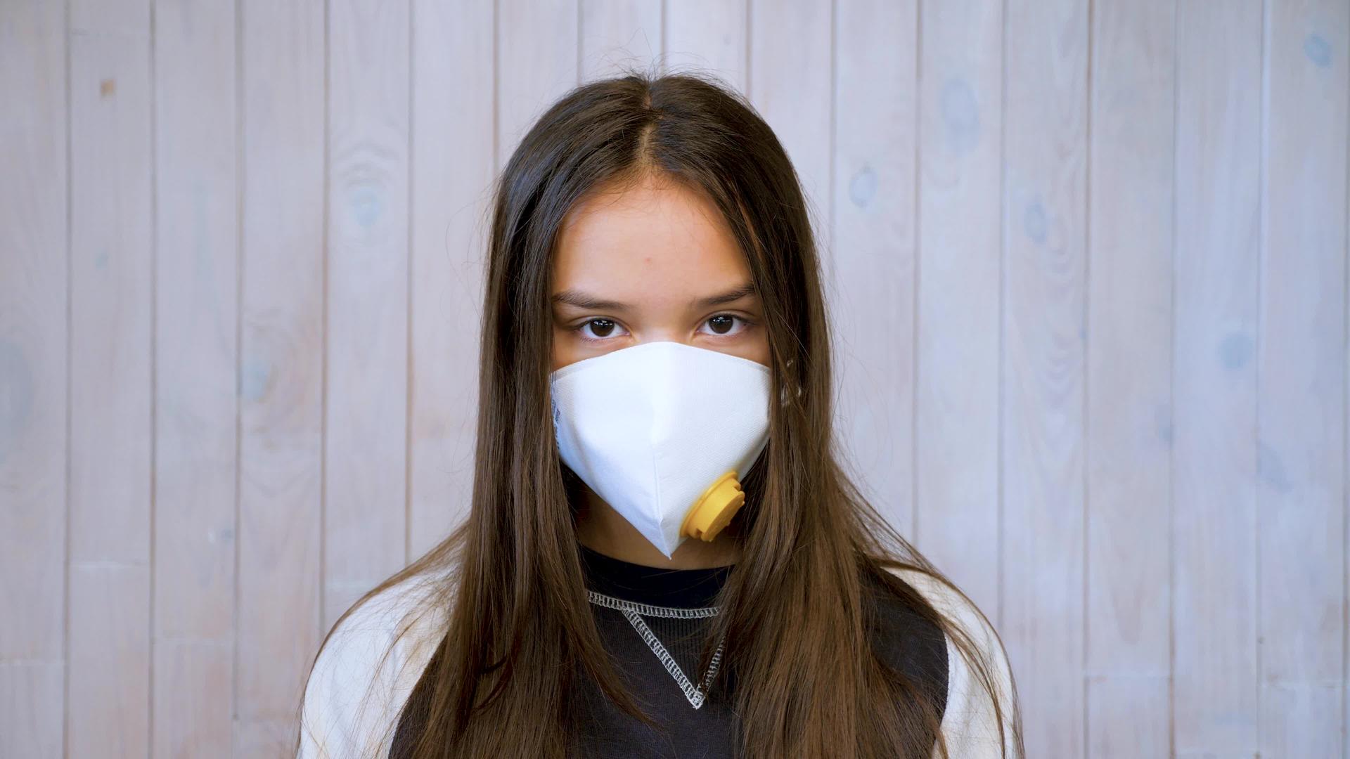 戴着医用防护口罩的十几岁女孩看着相机爆发墙壁浅灰色视频的预览图