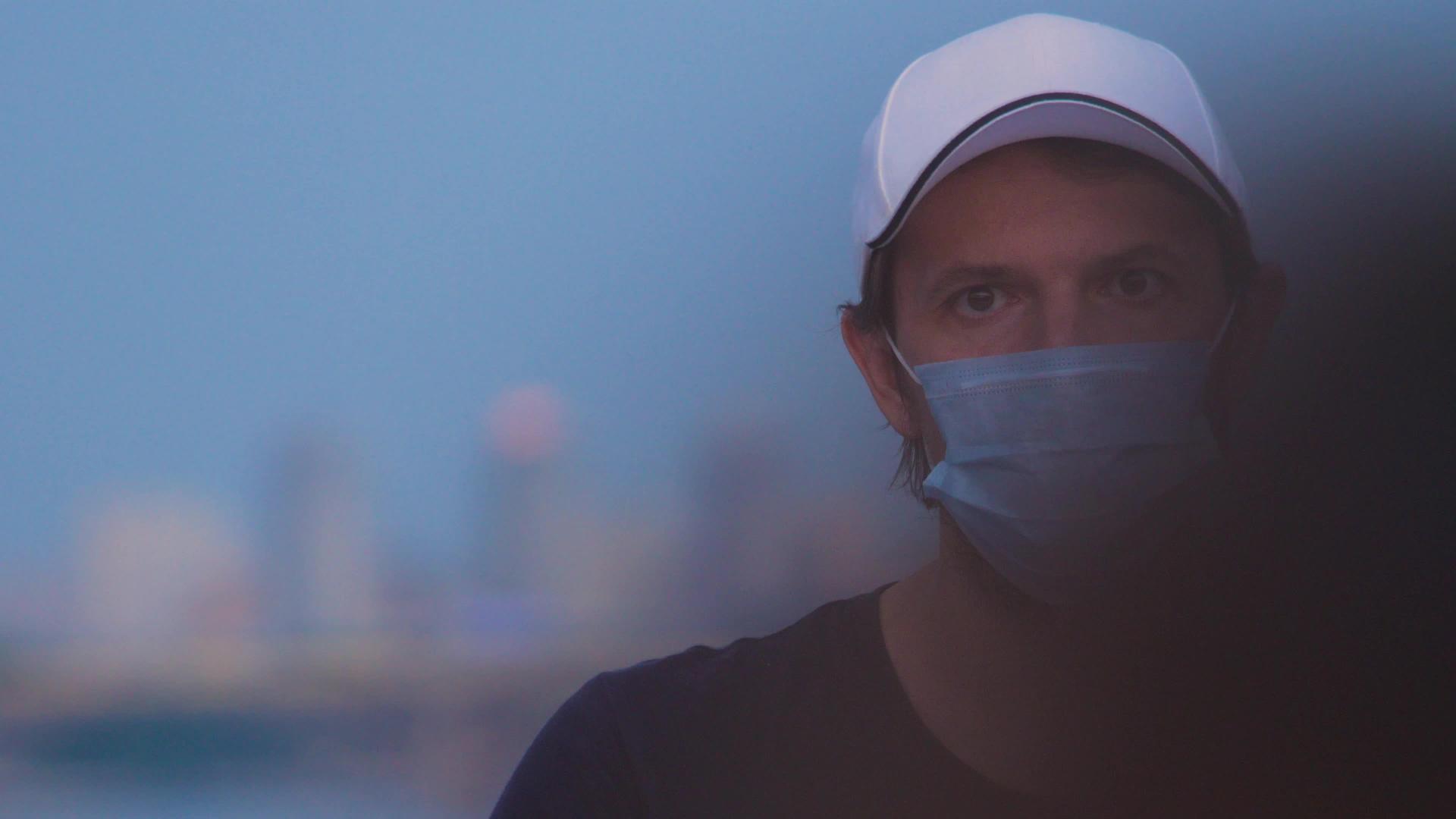 在城市背景下戴着防护医用口罩的男性戴着帽子和医用口罩视频的预览图
