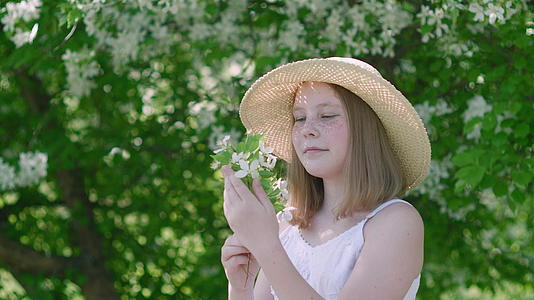 夏天一个浪漫的女孩在果园里戴着草帽手里拿着苹果树枝的肖像视频的预览图