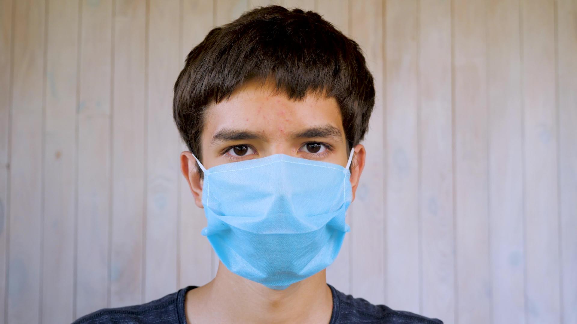 戴着医用口罩的男孩看着戴着口罩的17岁男孩的相机视频的预览图