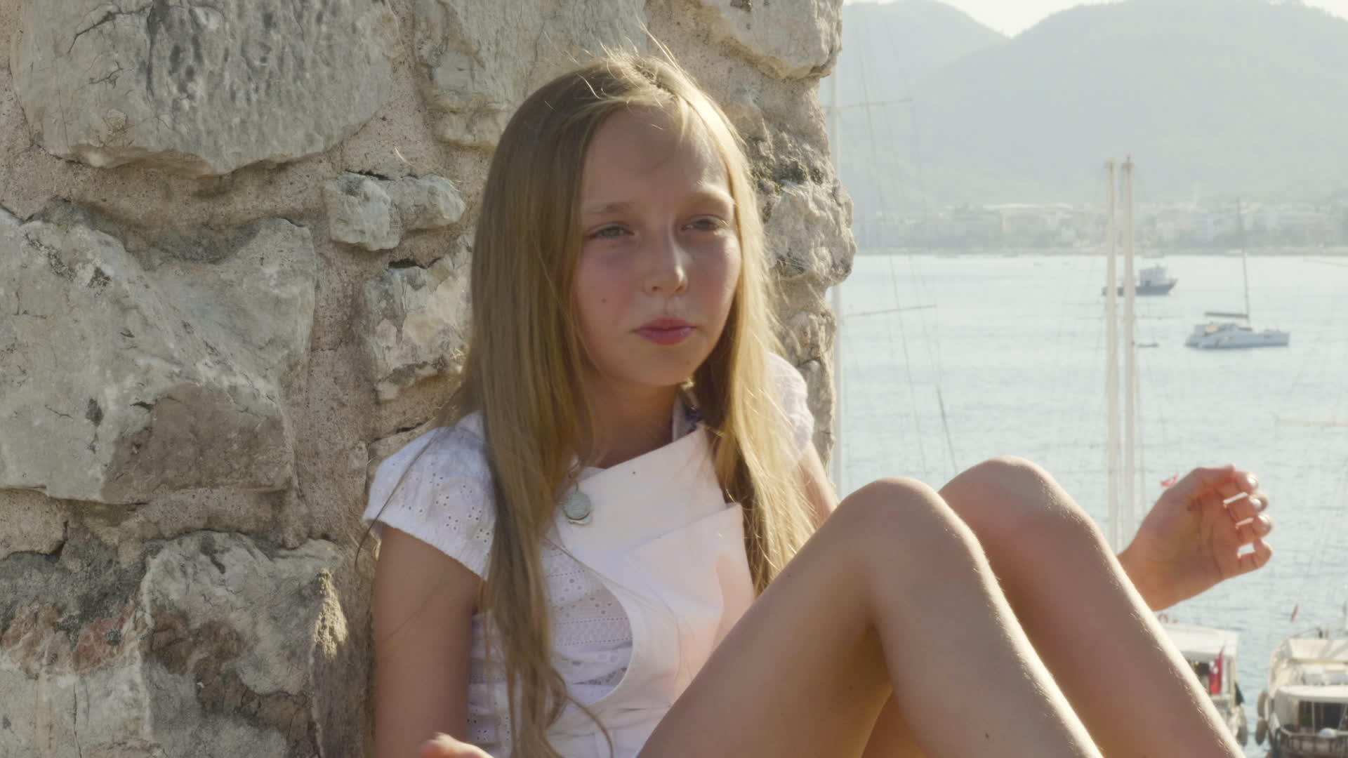 一个金发女孩坐在石墙和大海的背景下是一个快乐的女孩视频的预览图
