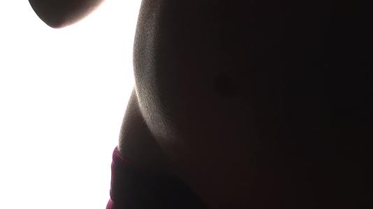 怀孕9个月后孕妇转身展示自己的肚子准备在白色背景背面做一个环视频的预览图