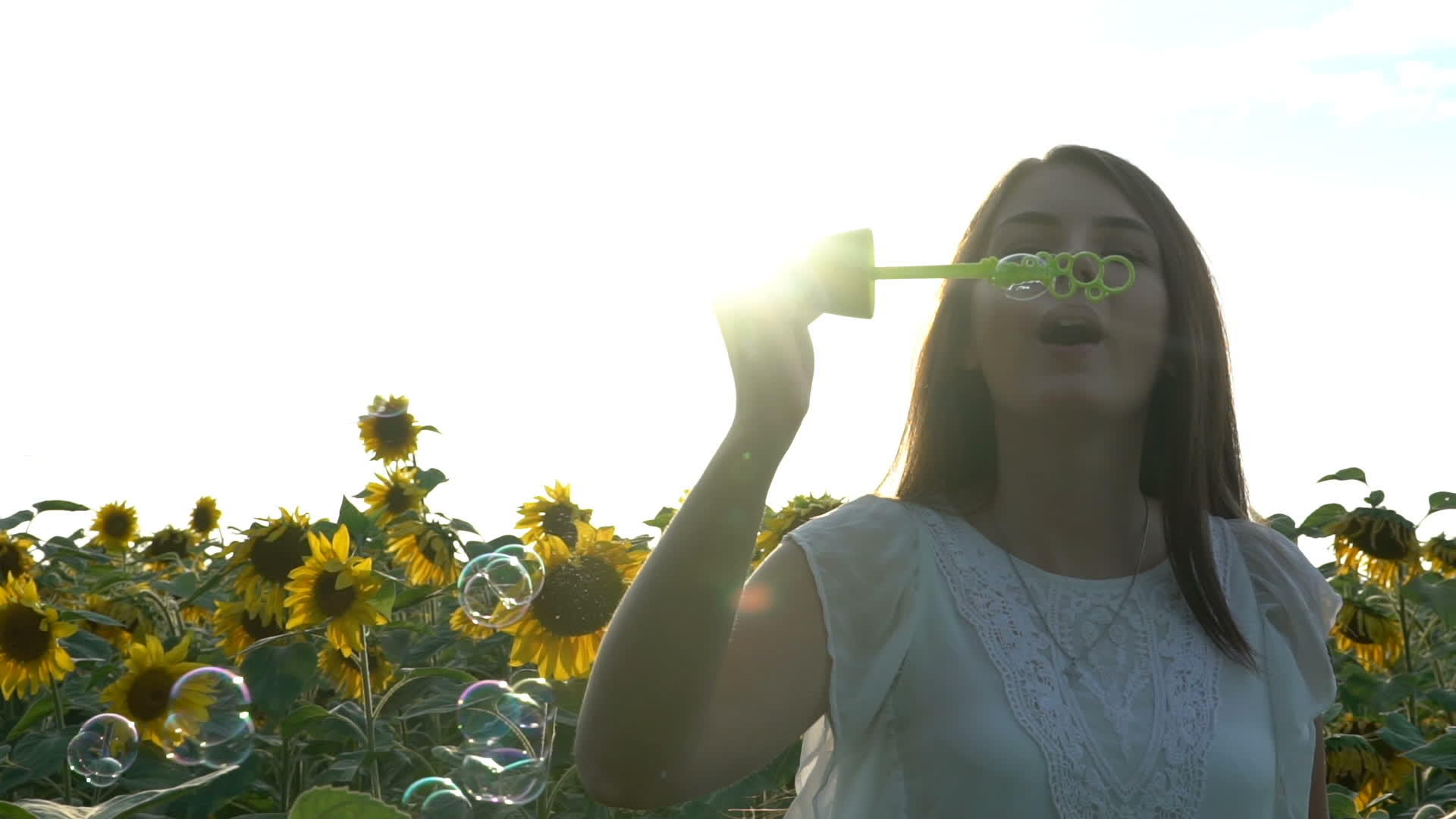 美丽的年轻女孩走在向日葵的黄色土地上吹着肥皂泡泡视频的预览图
