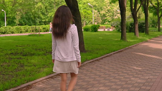 当妇女在城市公园里行走时在背面观看视频的预览图