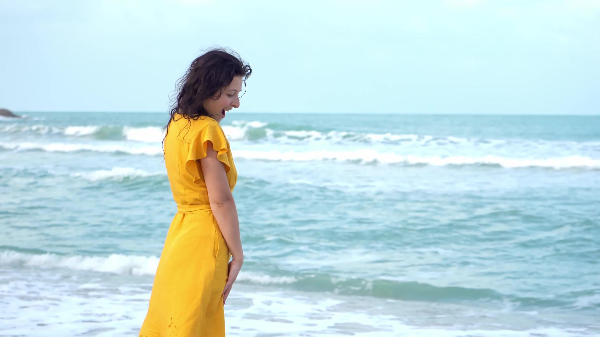 一个穿着黄色连衣裙的年轻漂亮的黑发女孩在海湾边缘视频的预览图