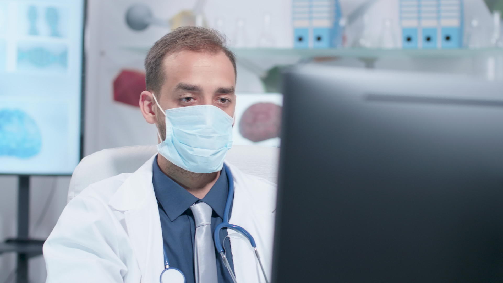 手持枪拍摄医生戴着药用面具在电脑上工作视频的预览图