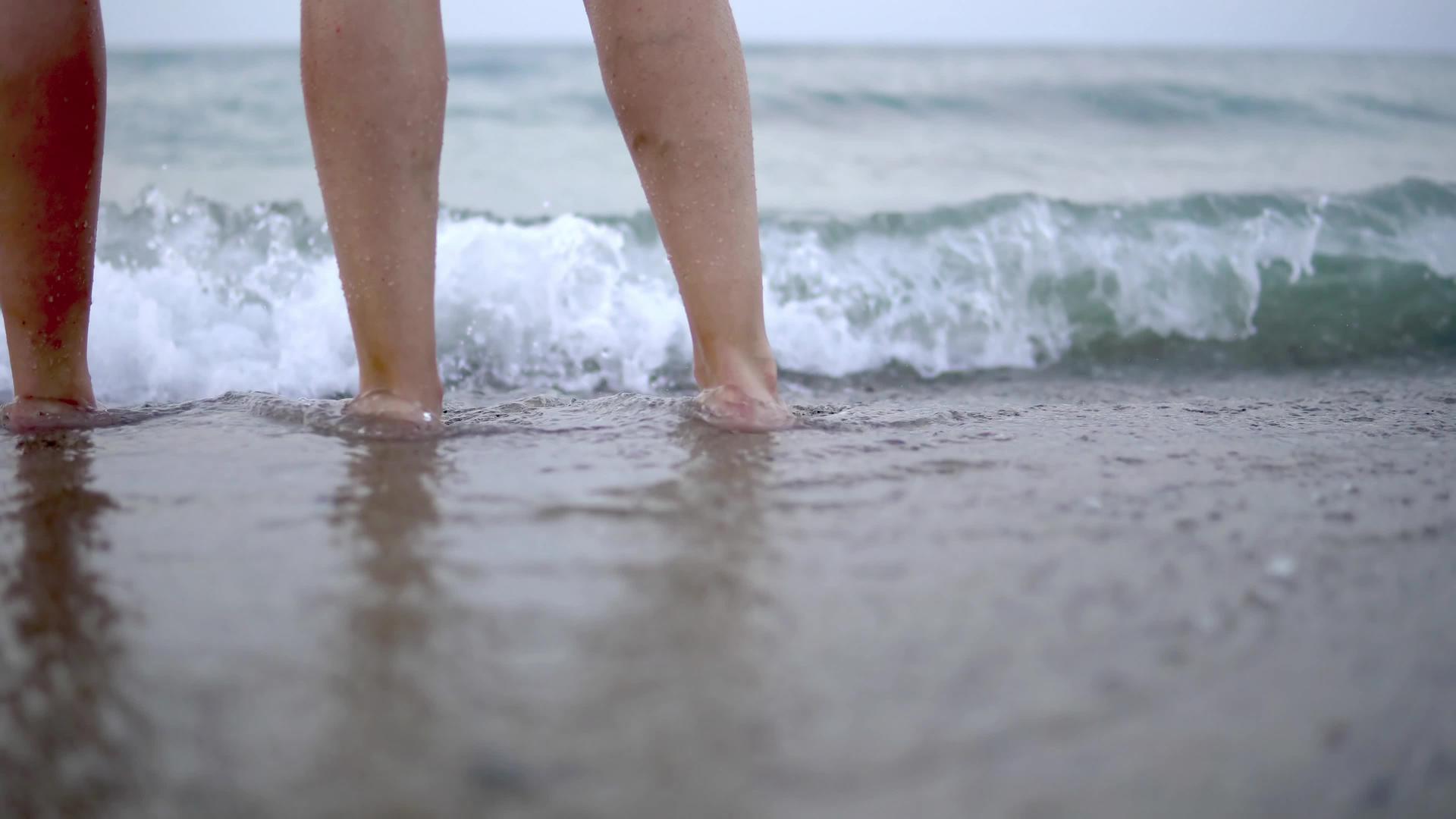 两对双脚站在沙滩上等待海浪的到来在沙滩上挥手视频的预览图