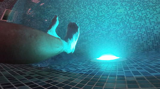 深黑的游泳池灯光和一双双脚在水下夜晚的大气中照亮视频的预览图