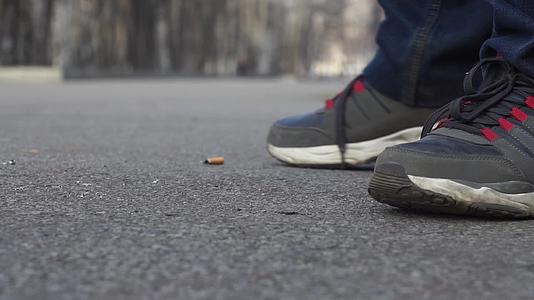 一名男子穿着运动鞋和牛仔裤站在城市公园里抽烟视频的预览图
