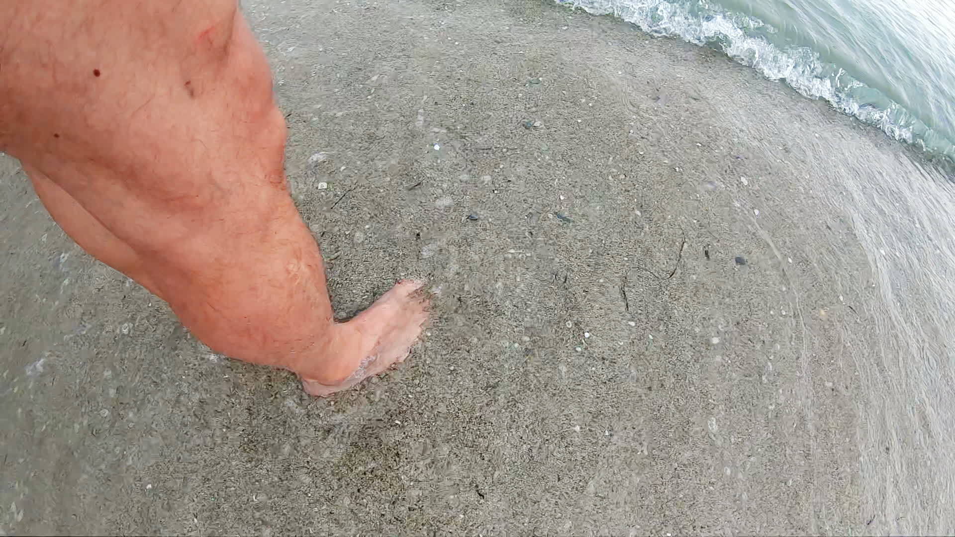 一个男人在浅海中挥舞着他的脚和波浪慢慢地撞击视频的预览图